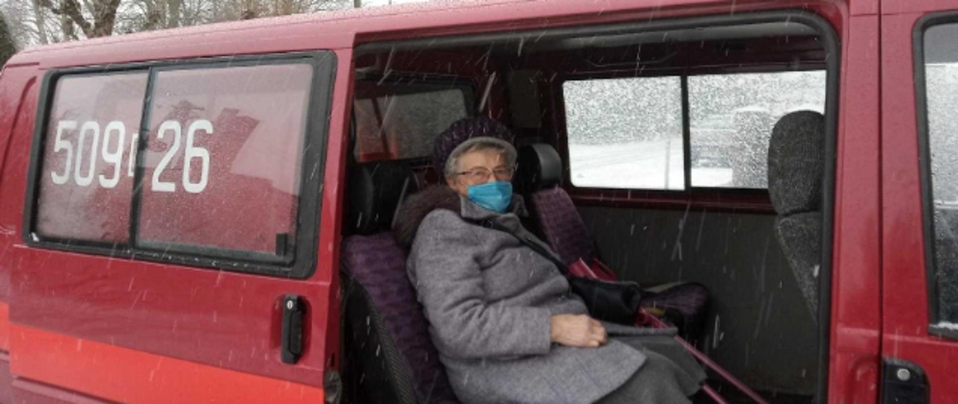 Pacjentka w maseczce siedzi w czerwonym samochodzie strażackim typu BUS z numerami operacyjnym 509 26 . Otwarte boczne drzwi przesuwne.