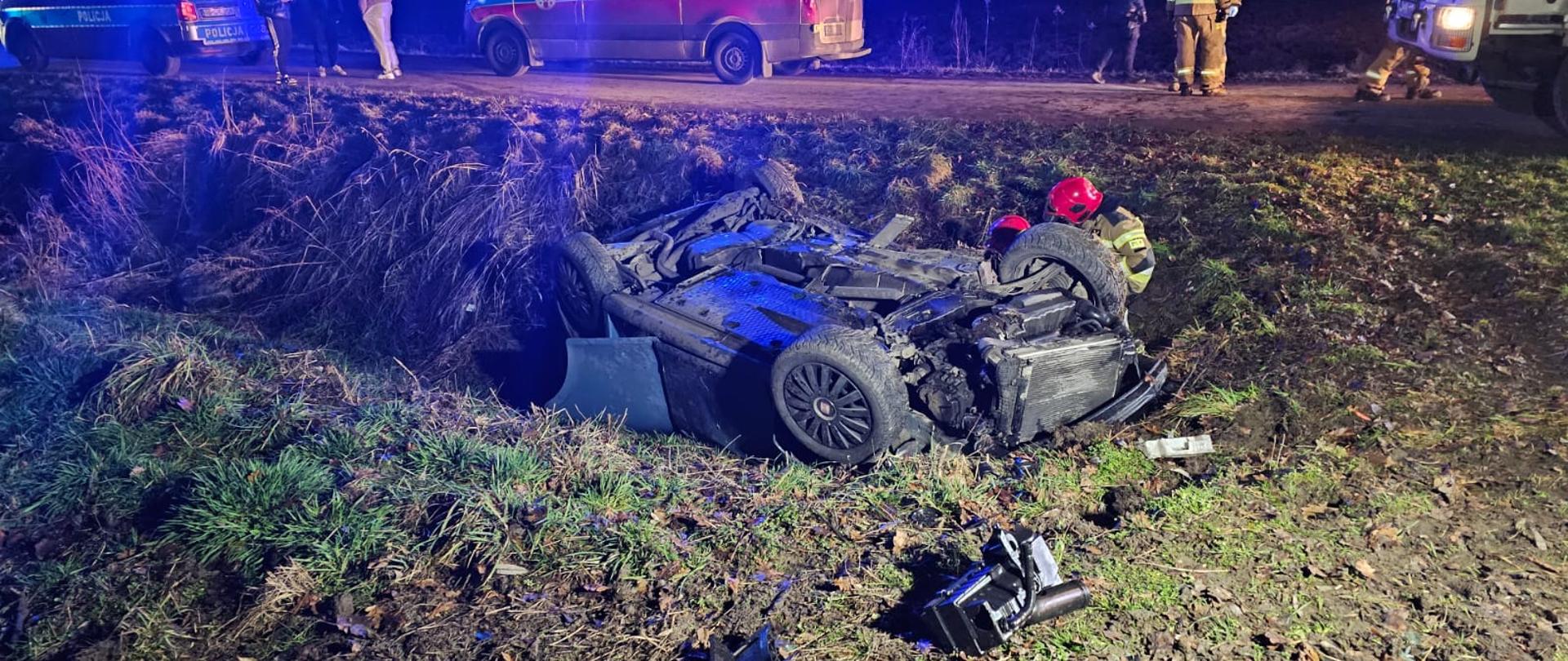Na zdjeciu widać dachowanie samochodu osobowego , pojazd na dachu w rowie, na drodze strażacy i ich pojazdy.