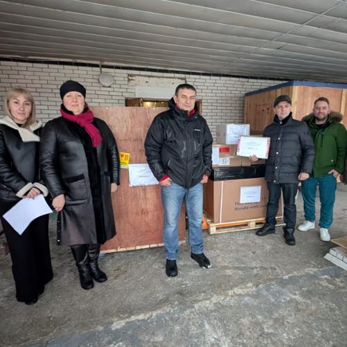 Grupa kobiet i mężczyzn stoi na tle palet z paczkami