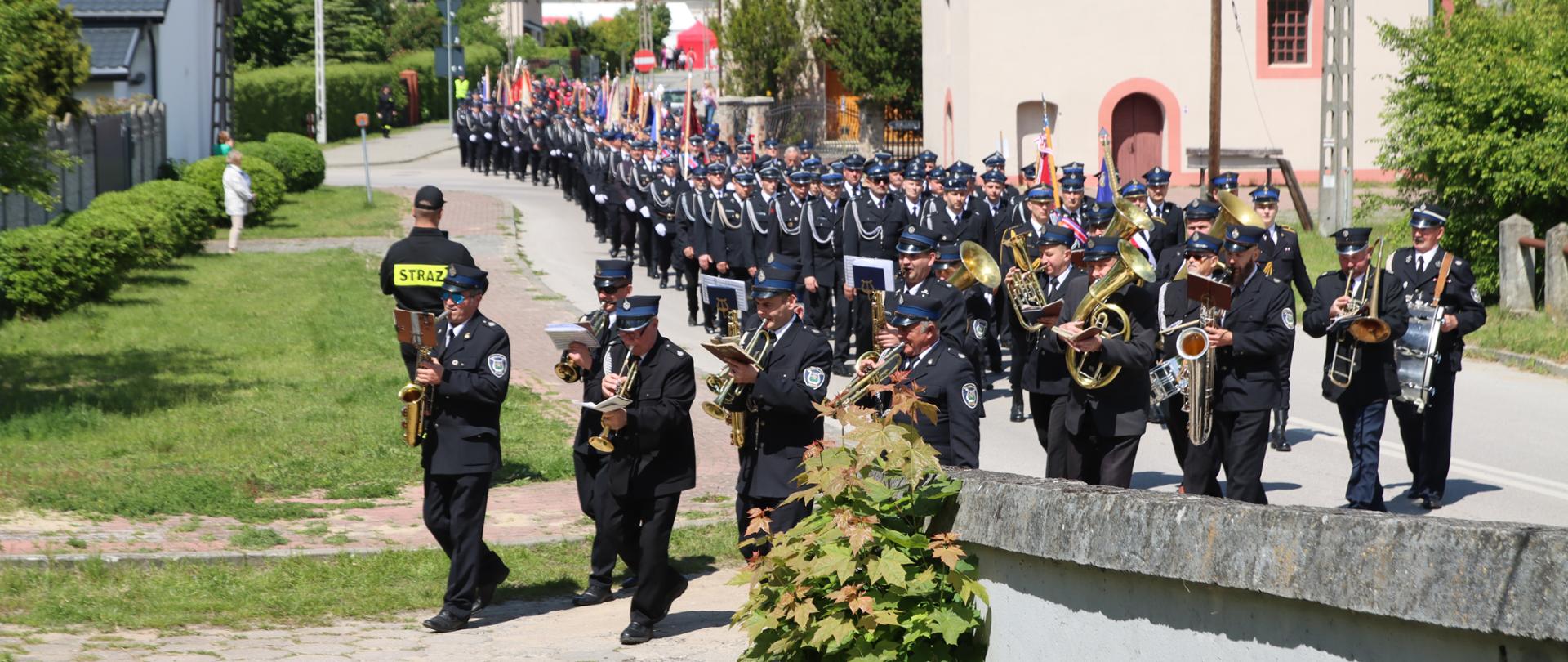 Przemarsz pododdziałów ulicami Sulejowa na pierwszym planie orkiestra dęta, w dalszym planie kompania i pododdział pocztów sztandarowych