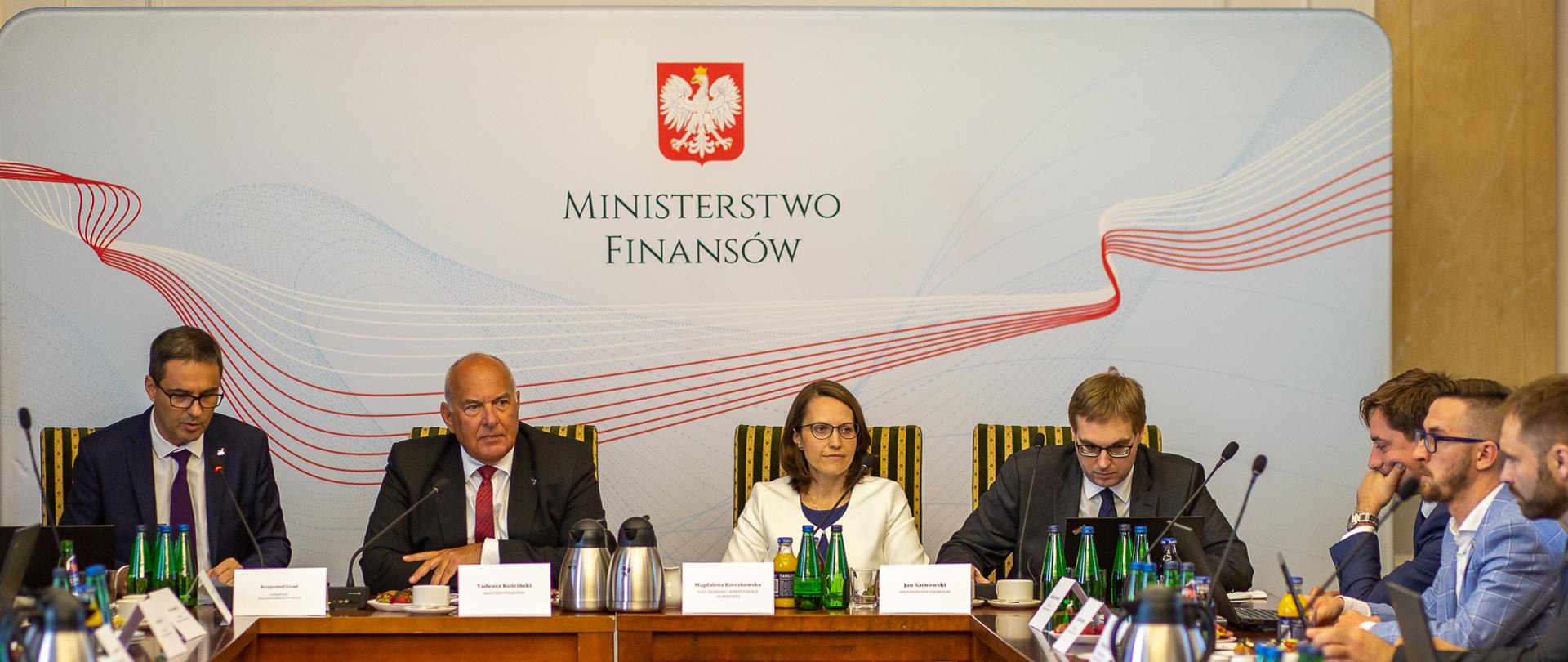 Od lewej: dyr. Biura Komunikacji i Promocji K. Grad, minister T. Kościński, szefowa KAS M. Rzeczkowska i wiceminister J. Sarnowski podczas śniadania prasowego siedzą za stołem, w tle baner z napisem Ministerstwo Finansów