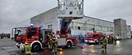 Zdjęcie przedstawia strażaków, podczas ćwiczeń na terenie zakładu produkcyjnego w Chodzieży.
W tle budynki zakładu produkcyjnego.
