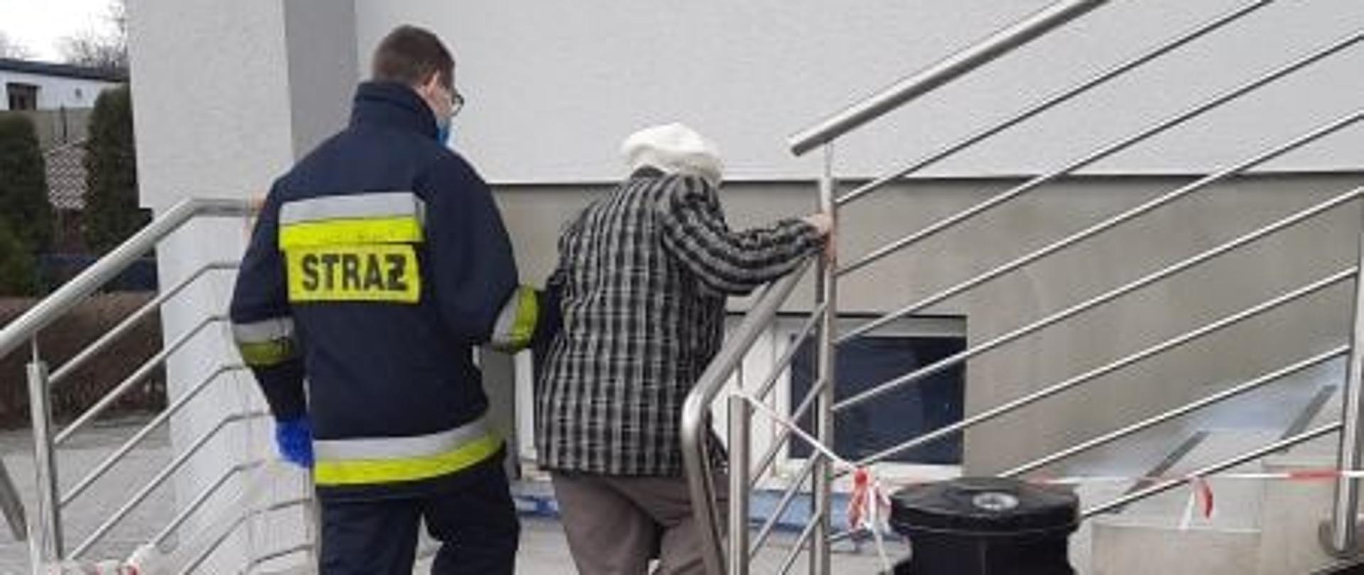 strażak pomaga osobie starszej podczas wchodzenia po schodach trzymając ją pod rękę