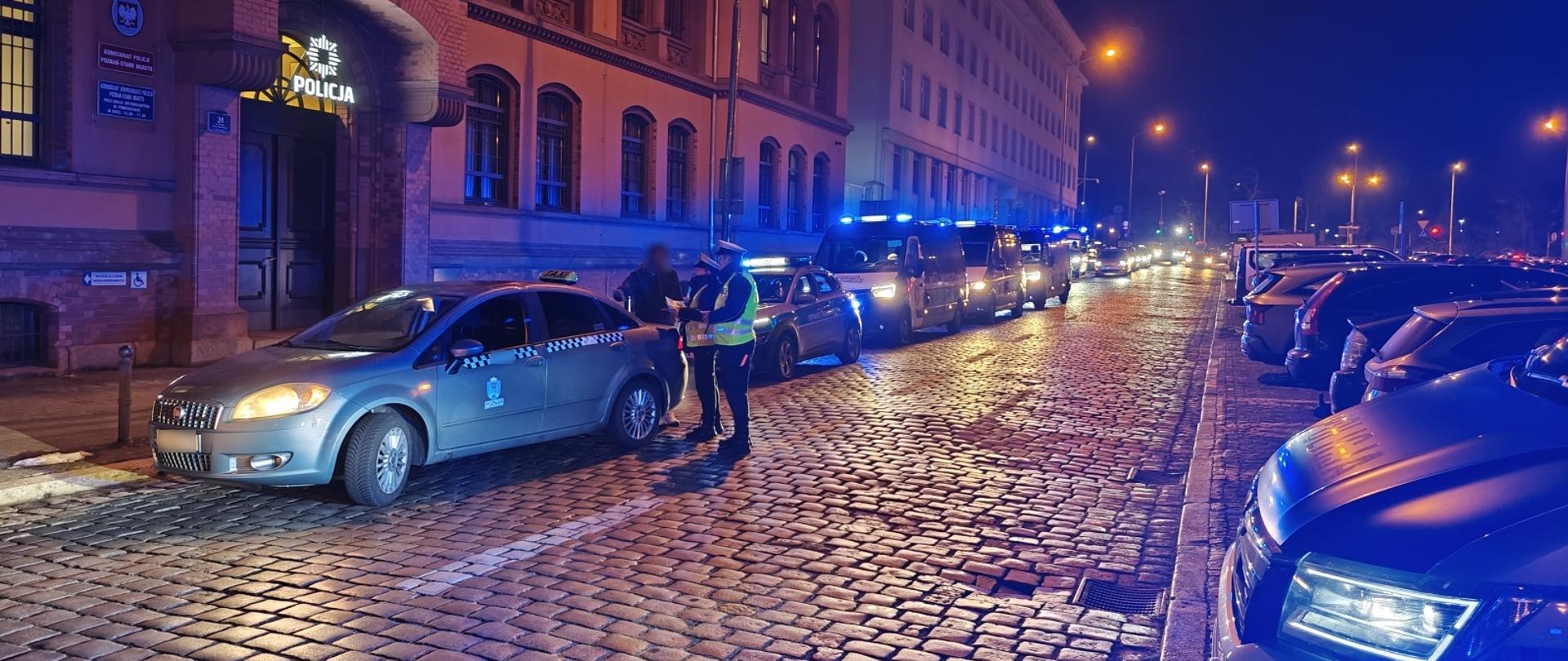 Taksówka poddawana kontroli na punkcie kontrolnym. Obok stojący inspektorzy transportu drogowego
