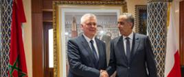 Na zdjęciu podający sobie ręce minister Tomasz Siemoniak (po lewej) i dyrektor Hammouchi (po prawej). Po prawej stoi biało-czerwona flaga Polski, a po lewej czerwono-zielona flaga Maroka. Za flagami widać kolumny z kolorowymi wzorami. Za ministrami zdjęcie mężczyzny w złotej ramie.