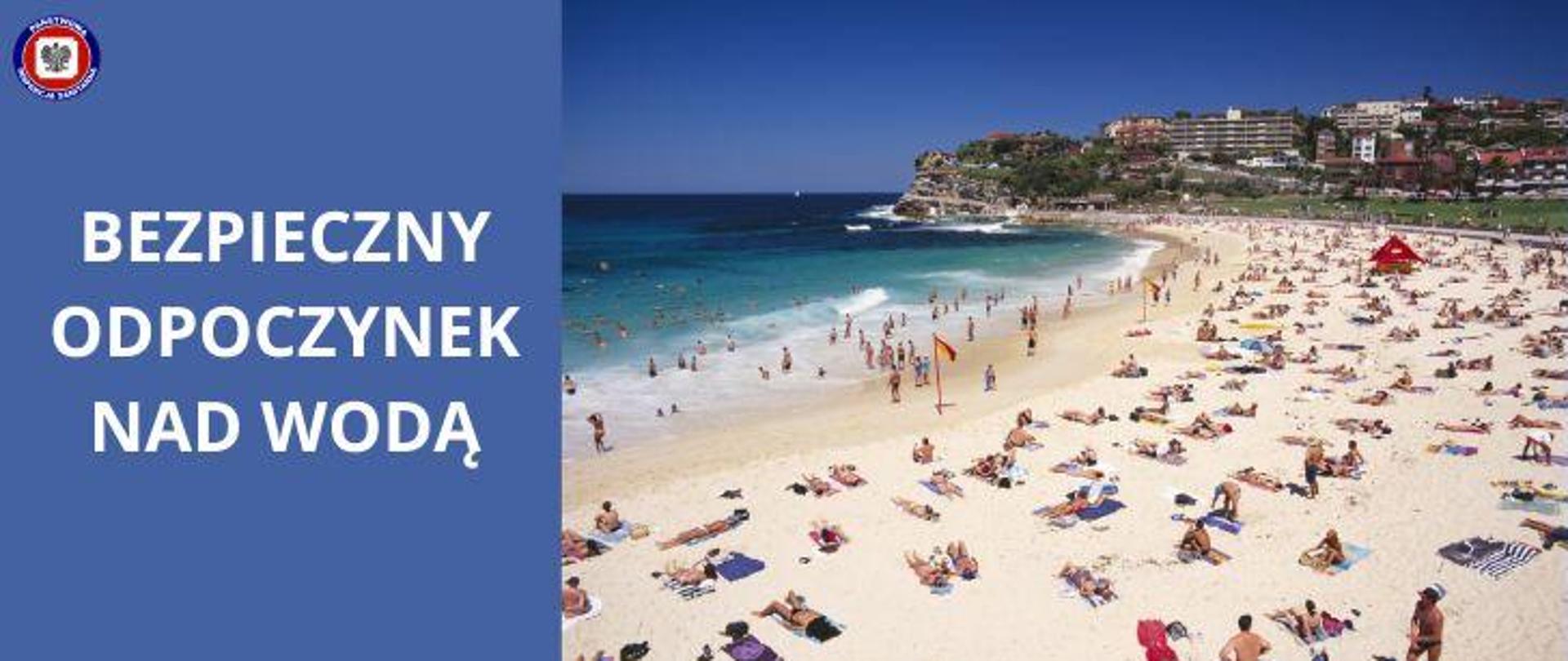 Po prawej na plaży leżą plażowicze korzystający z kąpieli słonecznej, w morzu kąpią się ludzie. Na horyzoncie miasto i budynki w pobliżu klifu. Po lewej na niebieskim tle jasny napis "Bezpieczny odpoczynek nad wodą". W lewym górnym rogu logo Państwowej Inspekcji Sanitarnej.