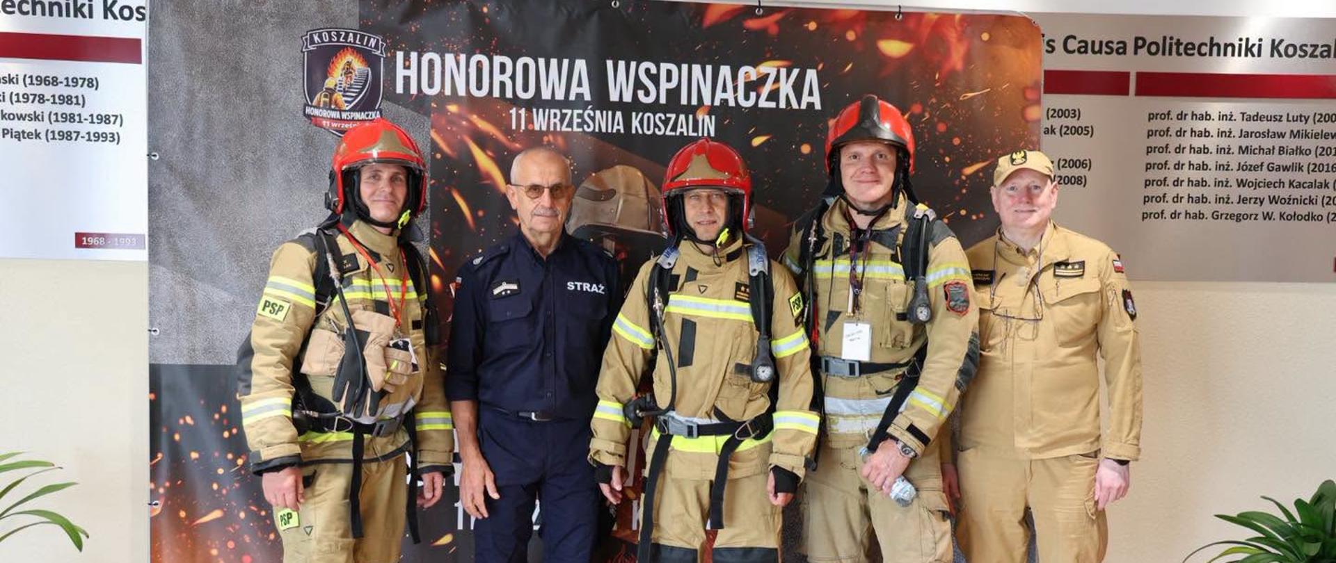 Uczestnicy Honorowej Wspinaczki Strażaków pozują do wspólnego zdjęcia na tle okolicznościowej ścianki promującej wydarzenie.
