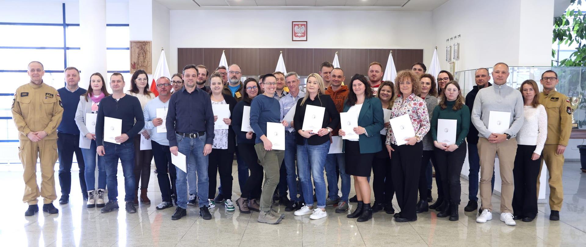 Pamiątkowe zdjęcie grupowe uczestników szkolenia inspektorów ochrony przeciwpożarowej (29 osób) w towarzystwie kobiety oraz dwóch oficerów CS PSP