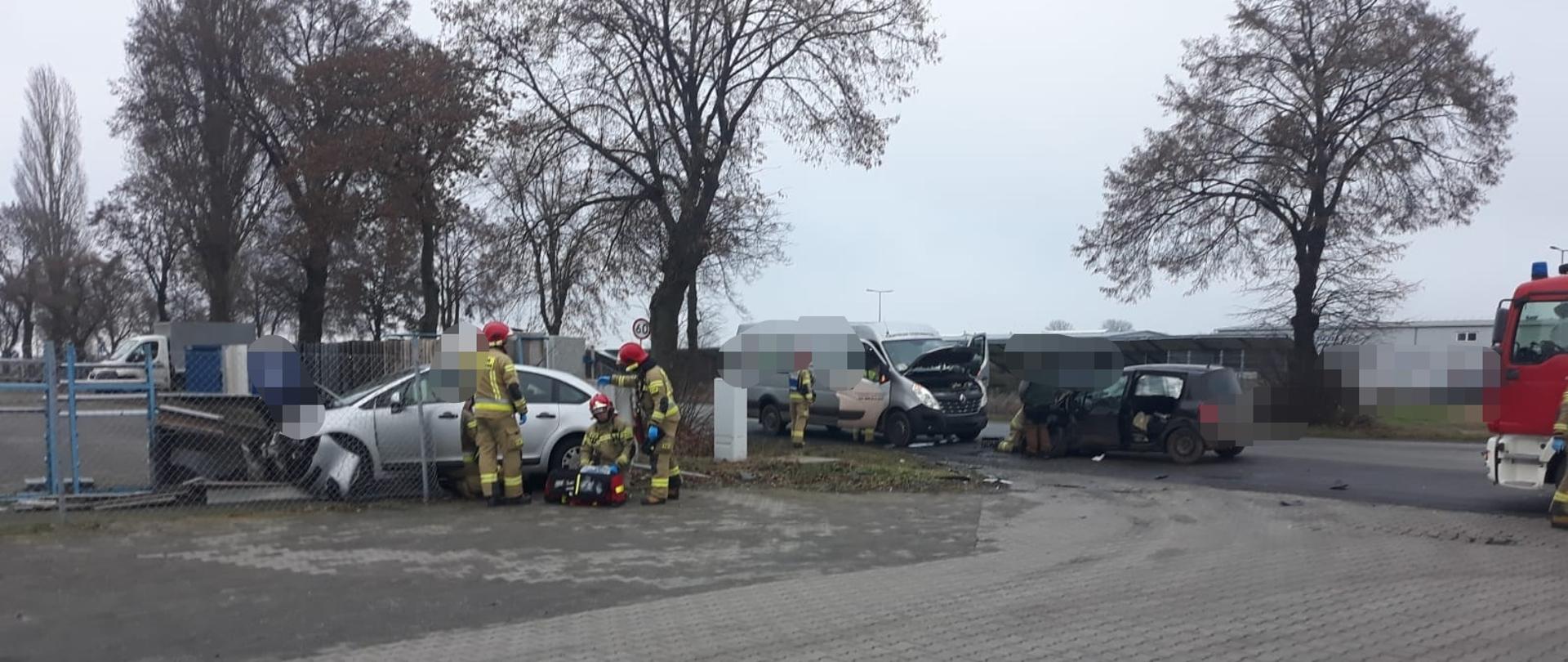 ZDERZENIE TRZECH POJAZDÓW. Na zdjęciu rozbite pojazdy biorące udział w zdarzeniu, strażacy udzielają pomocy osobom poszkodowanym.