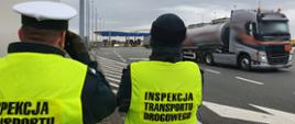Inspektorzy stoją w odblaskowych kamizelkach koło autostrady A2 i typują przejeżdżające ciężarówki do kontroli drogowych.