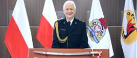 Odchodzący na emeryturę oficer PSP prezentuje otrzymaną z tej okazji okolicznościową szablę oficerską wraz z pochwą umieszczoną na brązowym tablo. W tle flagi stojące na stojakach
