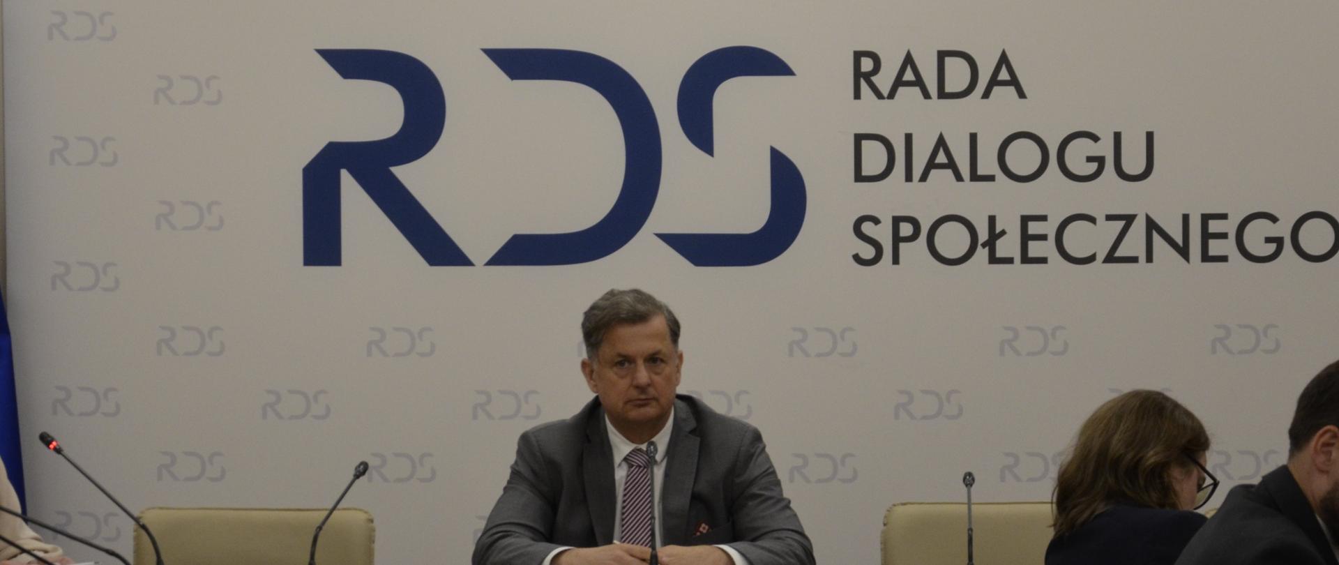 Na zdjęciu widnieje stół prezydialny za którym siedzi Pan Marcin Kolasa, Przewodniczący doraźnego Zespołu problemowego ds. służb mundurowych. W tle znajduje się baner z napisem Rada Dialogu Społecznego
