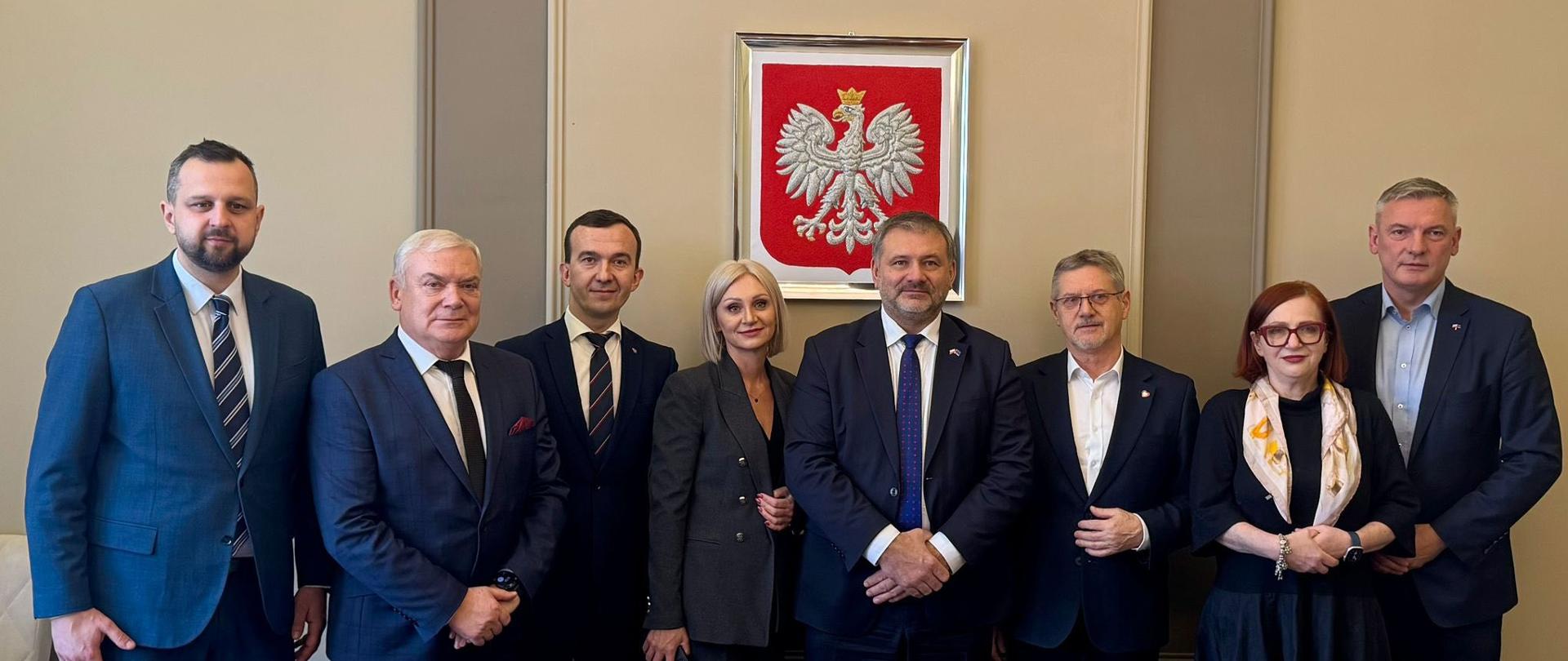 Grupa oficjeli pozuje do zdjęcia na tle orła białego