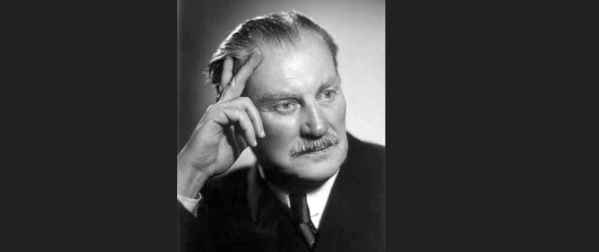 Czarno-biała fotografia portretowa prof. Władysława Szafera, ukazująca go w zamyśleniu – z uniesioną ręką opartą o skroń, w eleganckim garniturze i z charakterystycznym wąsem. Zdjęcie wykonane w klasycznym stylu lat międzywojennych, podkreślające skupienie i intelektualną charyzmę uczonego, który odegrał kluczową rolę w rozwoju botaniki, ochrony przyrody i szkolnictwa wyższego w Polsce.