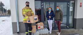 Strażak przekazujący środki ochrony indywidualnej personelowi punktu szczepień.