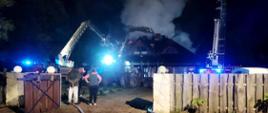 Pożar budynku mieszkalnego - Męciszów. Na zdjęciu dym wydobywający się z dachu budynku. Obok stoją rozstawione podnosniki.