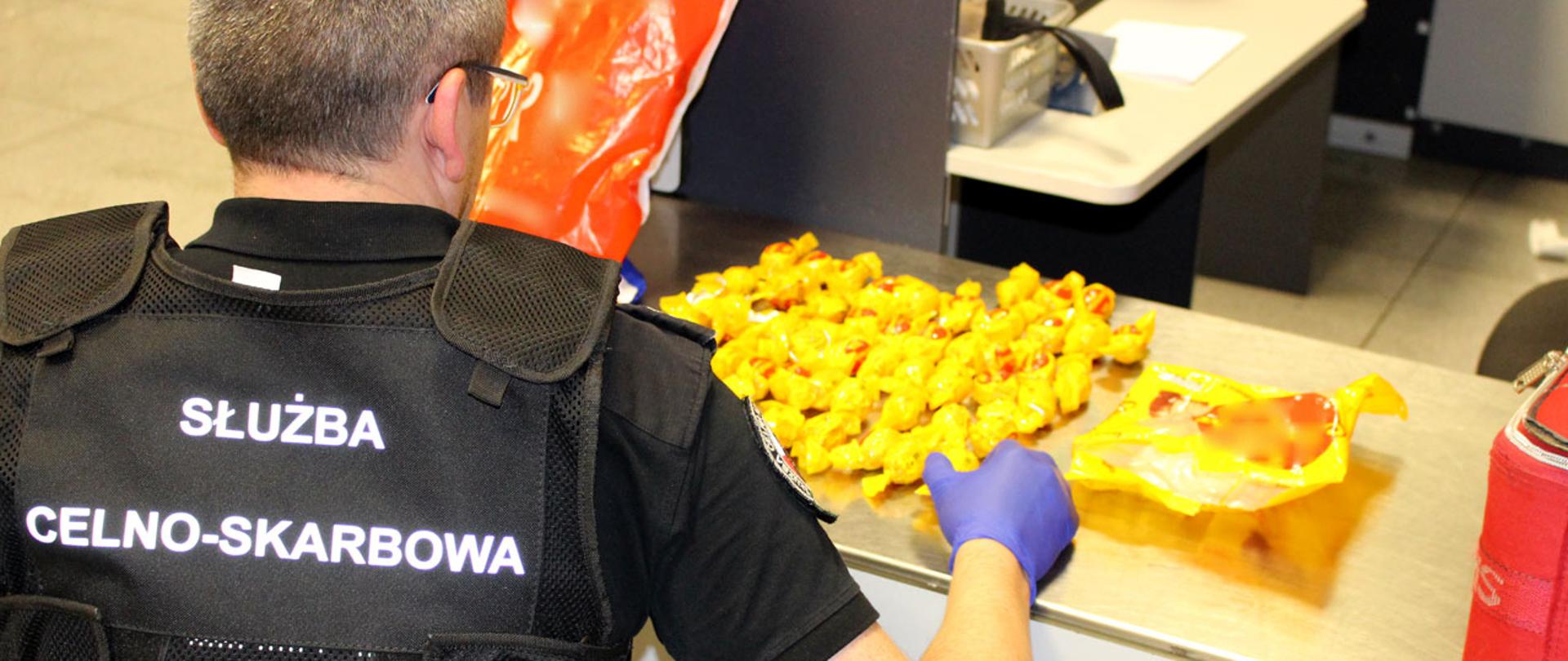 Funkcjonariusz Służby Celno-Skarbowej przy rozłożonych na blacie żółtych cukierkach.
