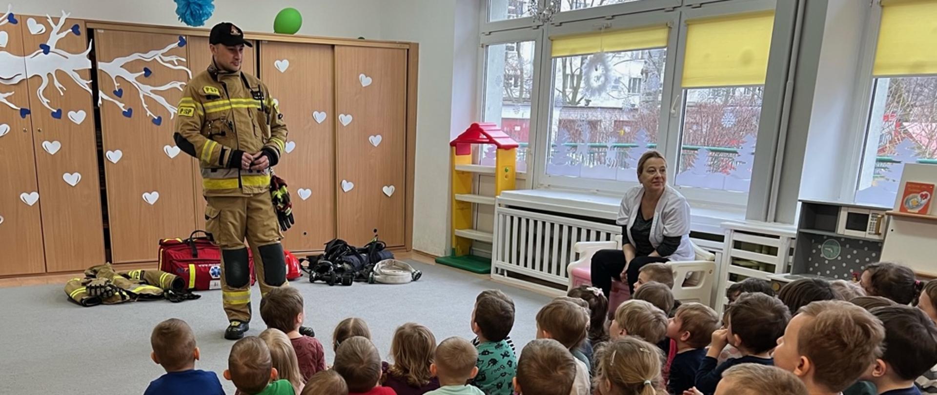 Strażak z JRG 5 w przedszkolu, stojący przed siedzącymi dziećmi