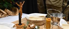 Na stoliku stoi krzyż, obok sianko ze żłobkiem i Panem Jezusem w koszykach znajdują się białe opłatki. Na stole stoją też dwie zapalone świece