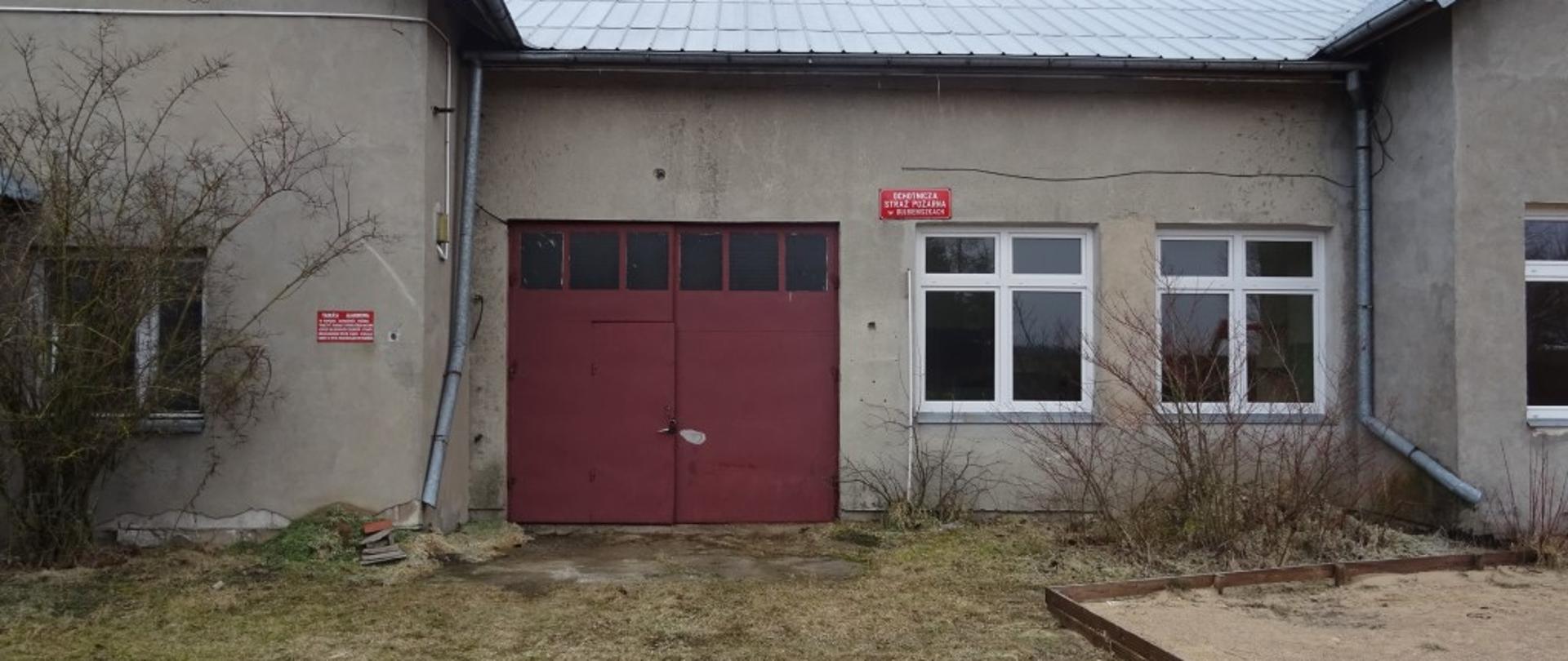Budynek murowany koloru szarego kryty blachą. Brama garażowa koloru czerwonego. Podjazd utwardzony z ziemi. 