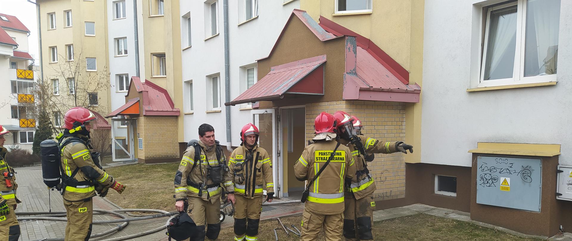 Strażacy przed klatką schodową po zlokalizowaniu pożaru