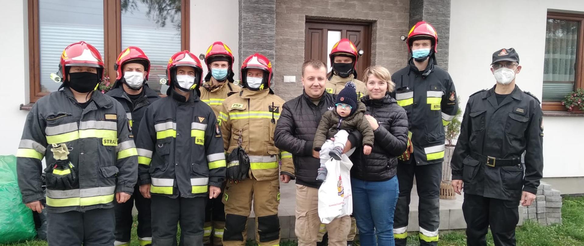Zdjęcie przedstawia Ignasia z rodzicami, oraz zmianę służbową z komendantem powiatowym Państwowej Straży Pożarnej w Wąbrzeźnie st.bryg. mgr inż. Januszem Woźniakiem na czele. Zdjęcie wykonane na tle domu Ignasia.