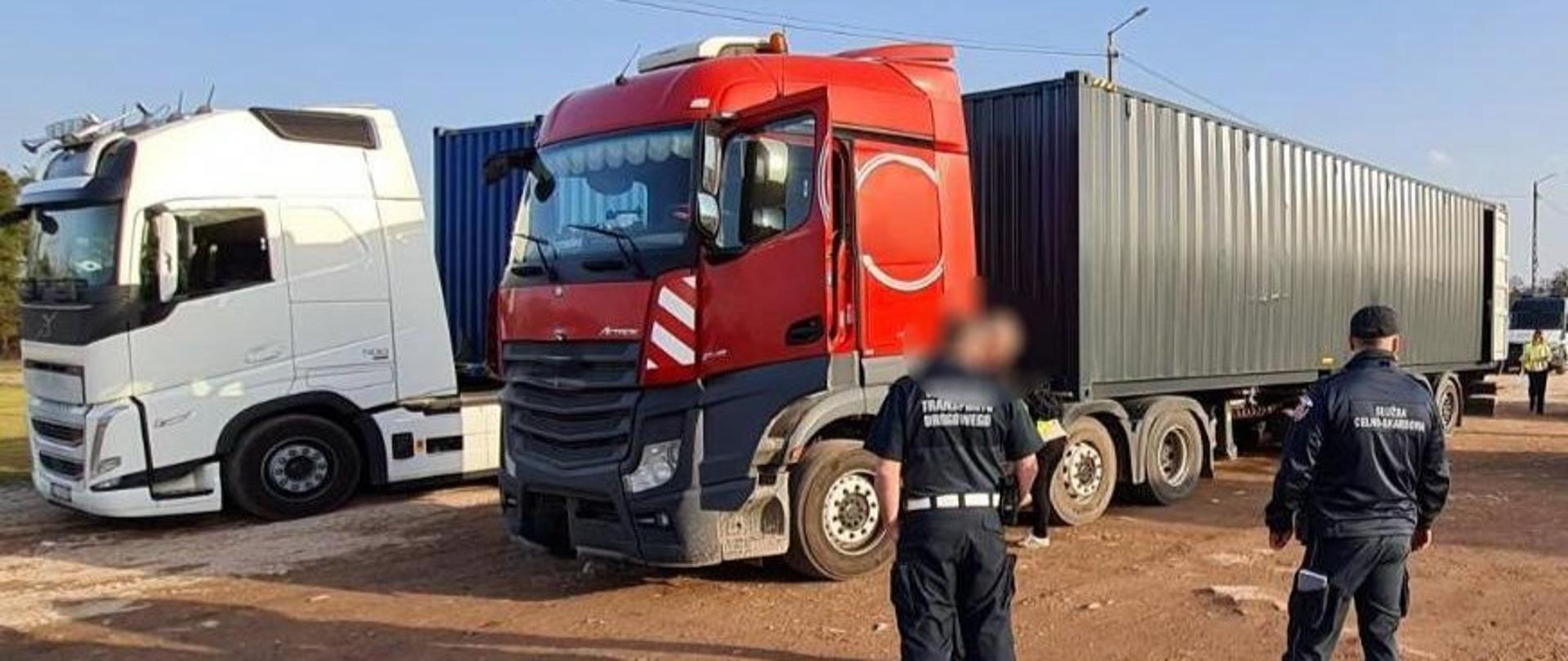 Dwie ciężarówki z naczepami kontenerowymi; w pobliżu pojazdu znajdują się osoby w mundurach.