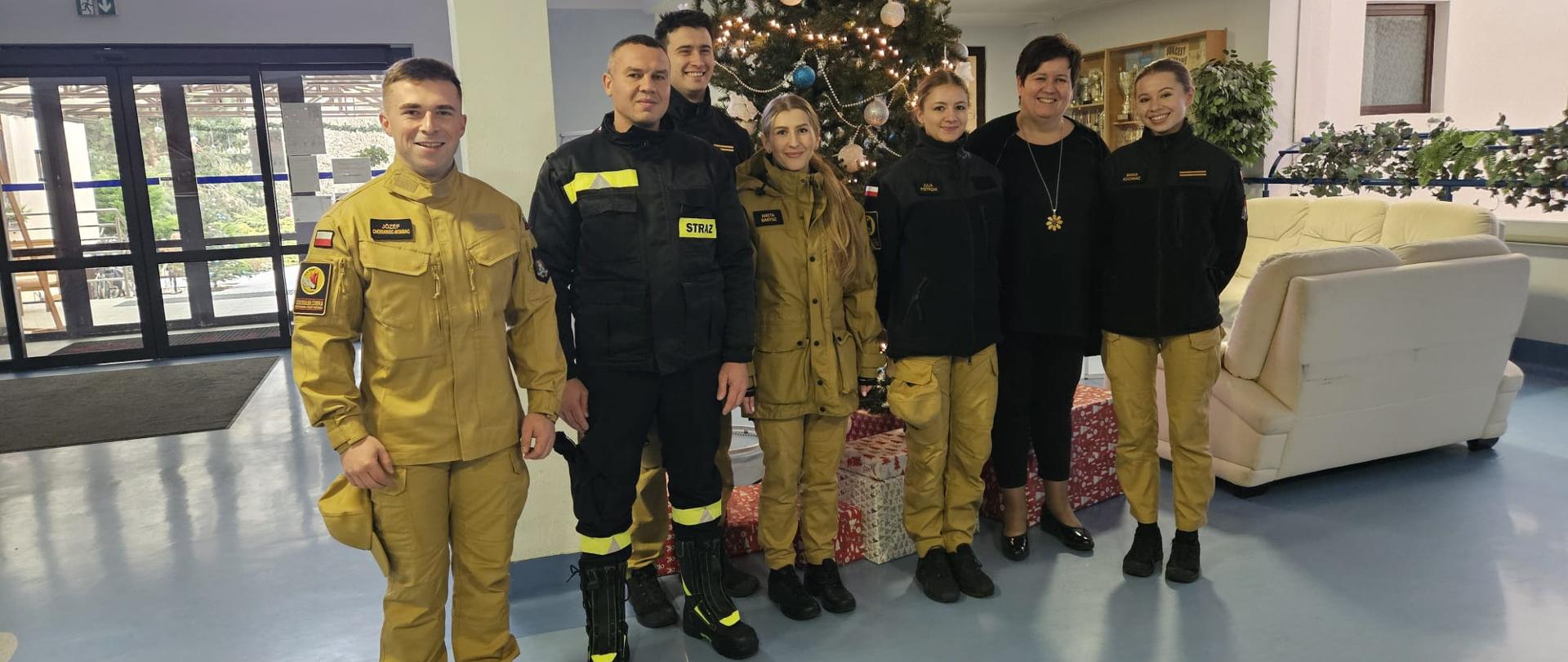 Kadeci Centralnej Szkoły PSP wraz z panią gospodarz stojący w szeregu w holu budynku na pamiątkowy zdjęciu grupowym . W tle udekorowana świąteczna choinka