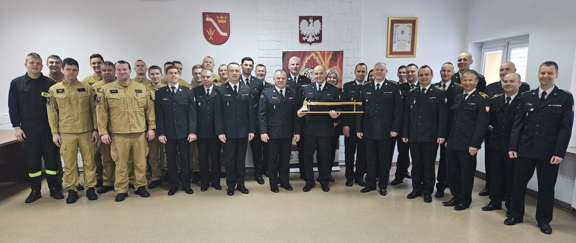 strażacy stoją do zdjęcia na tle godła