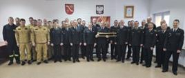 Pożegnanie ze służbą - strażacy stoją na tle ściany z godłem