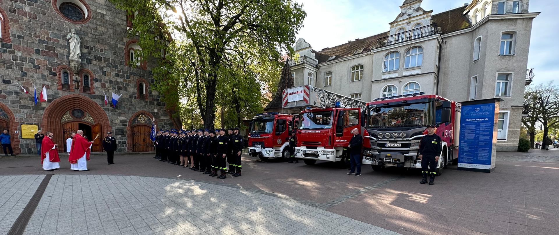 Strażacy w dwuszeregu pod kościołem. Ksiądz święci sprzęt i samochody używane przez strażaków