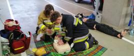 Na zdjęciu widoczni są strażacy-ochotnicy podczas praktycznego egzaminu szkolenia podstawowego strażaków ratowników ochotniczej straży pożarnej. Strażacy potwierdzając swoje umiejętności z zakresu udzielania pierwszej pomocy.