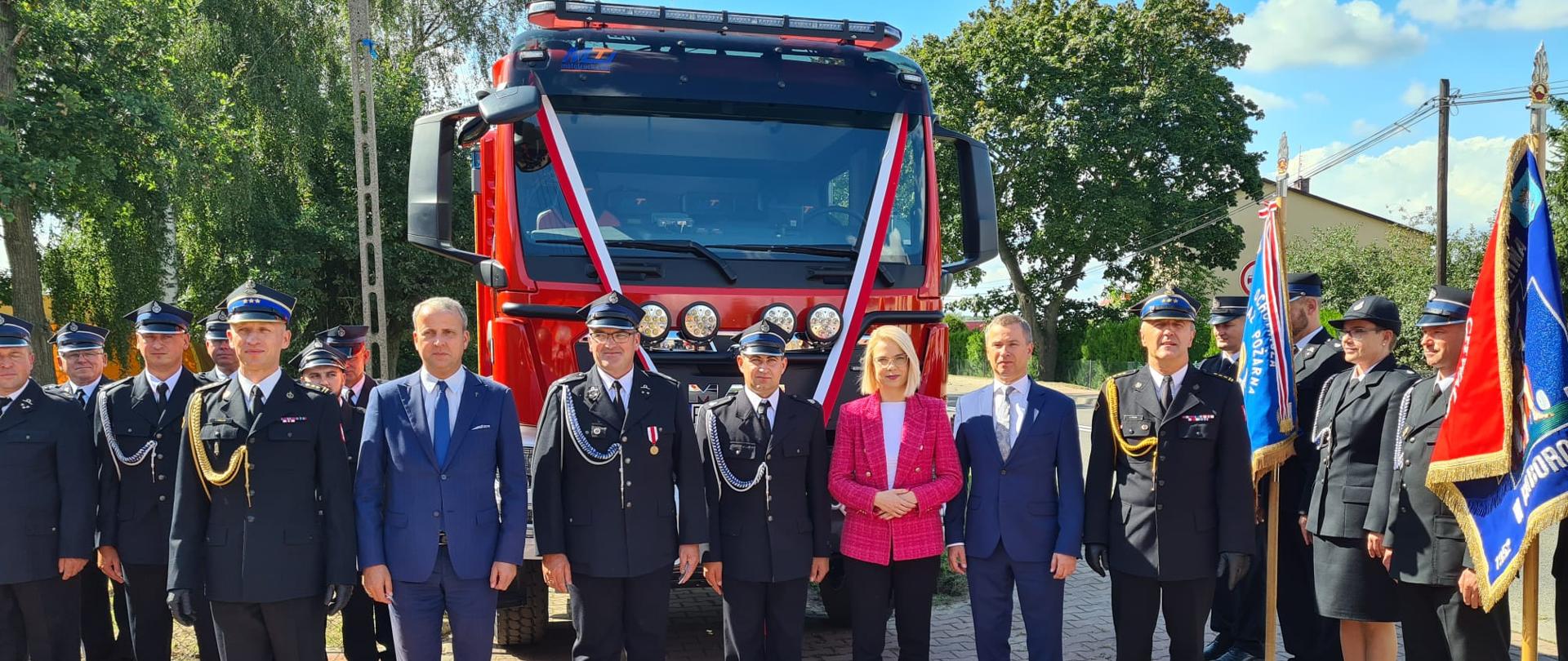 Pamiątkowe zdjęcie uczestników wydarzenia na tle nowego samochodu strażackiego