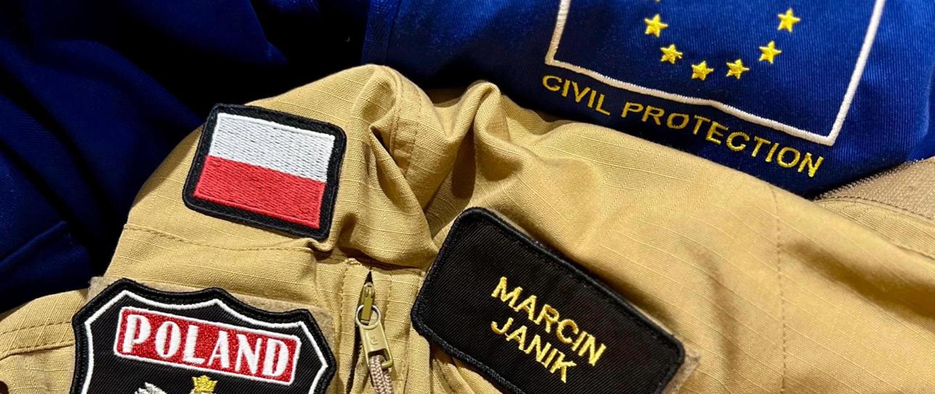 Element umundurowania z emblematami: Marcin Janik, kolejny z wizerunkiem godła Polski i napisem POLAND oraz POLISH ASSISTANCE, kolejny z napisem KG PSP, oraz na czerwonym tle napis World Health Organization