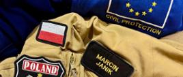 Element umundurowania z emblematami: Marcin Janik, kolejny z wizerunkiem godła Polski i napisem POLAND oraz POLISH ASSISTANCE, kolejny z napisem KG PSP, oraz na czerwonym tle napis World Health Organization