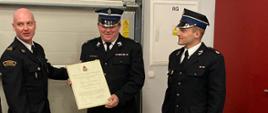 Zdjęcie przedstawia Komendanta Powiatowego PSP w Jędrzejowie mł. bryg. Mariusza Stolarczyka, który wręcza przedstawicielom OSP Sędziszów decyzję o włączeniu do krajowego systemu ratowniczo-gaśniczego. Wszyscy strażacy w umundurowaniu galowym znajdują się na garażu jednostki OSP Sędziszów.