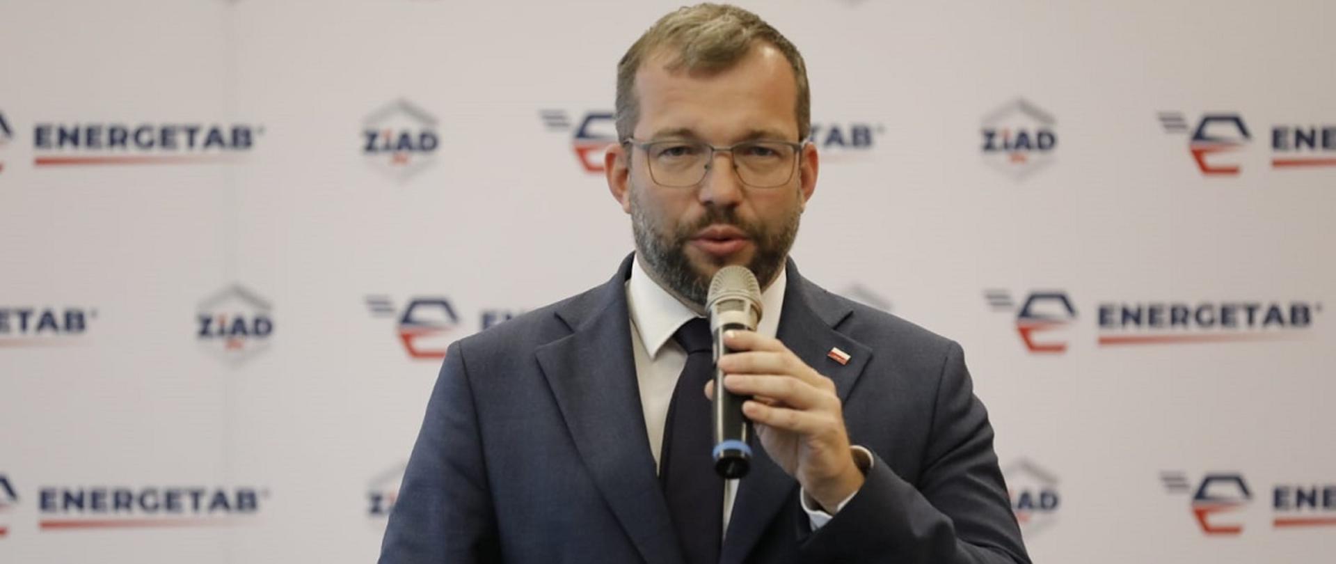 Minister funduszy i polityki regionalnej Grzegorz Puda przemawia do mikrofonu, za jego plecami baner targów