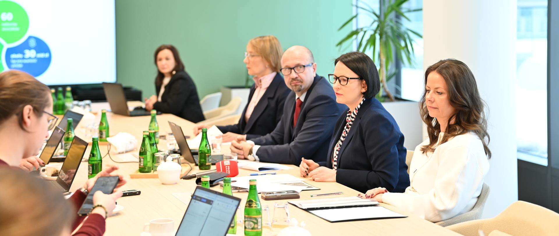 Na fotografii osoby siedzące przy stole po dwóch jego stronach. Spotkanie członków zarządu NFOŚiGW z dziennikarzami.