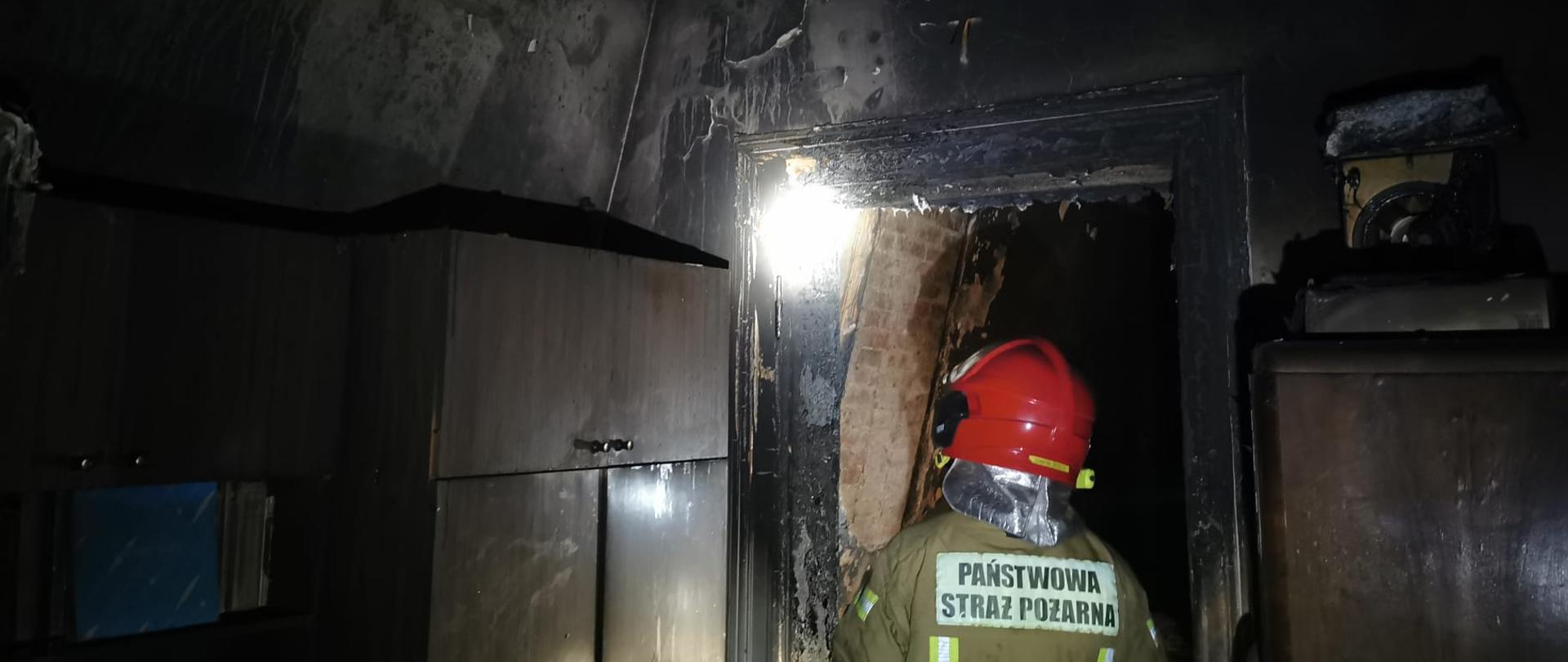 Na zdjęciu widać strażaka wewnątrz spalonego mieszkania 