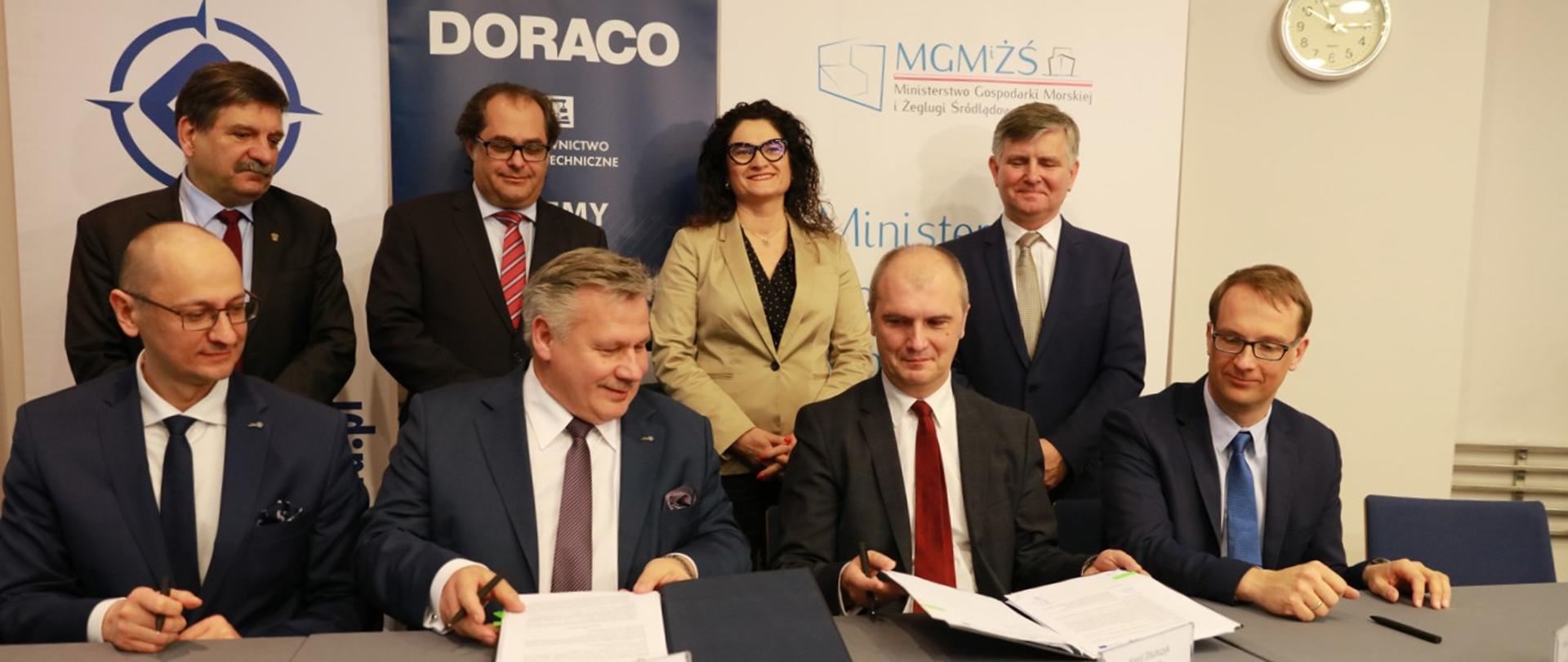 Prezes Portu Gdynia oraz przedstawiciel firmy Doraco podpisują umowę w tle min. minister M. Gróbarczyk
