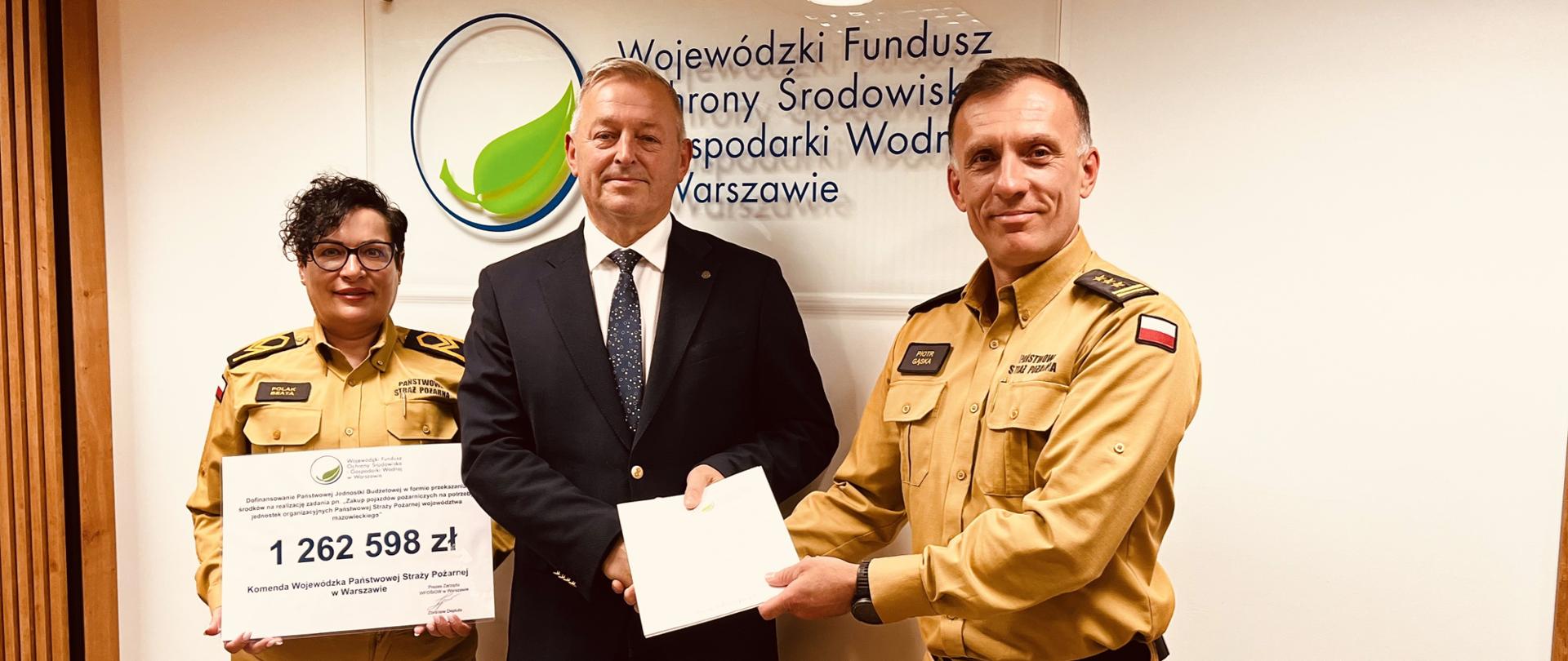 Zastępca Komendanta Wojewódzkiego PSP w Warszawie, Główna Księgowa PSP w Warszawie oraz Dyrektor WFOŚiGW w Warszawie prezentują podpisaną umowę na tle loga funduszu. 