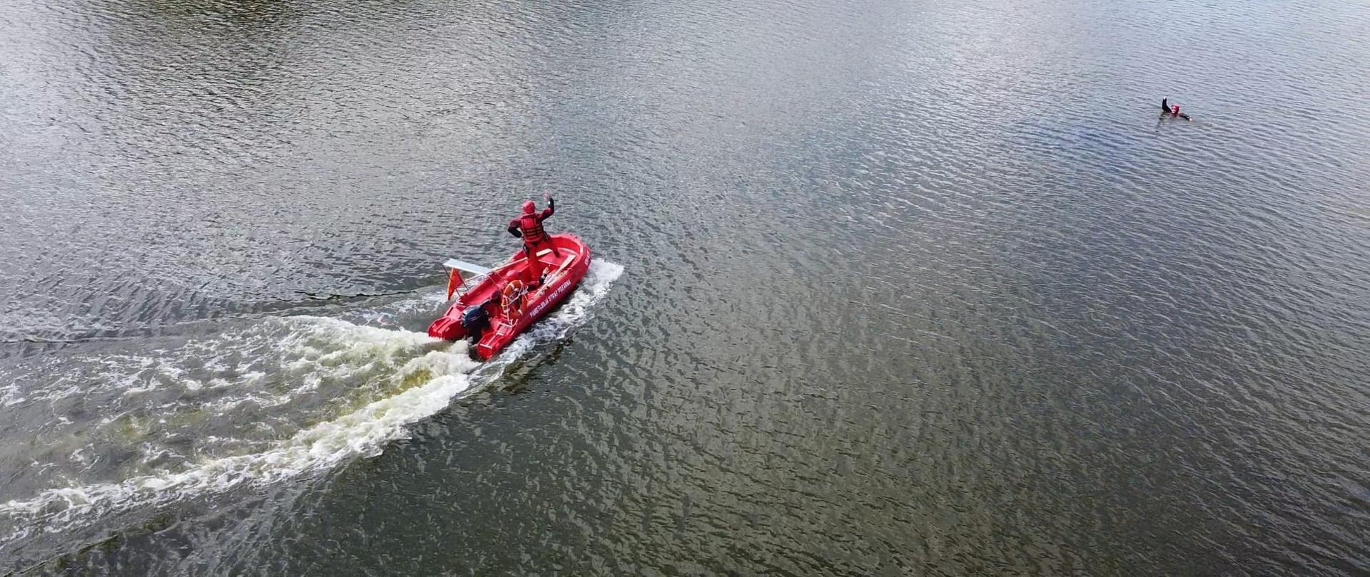 Strażacy łodzią ratowniczą płyną w kierunku osoby poszkodowanej