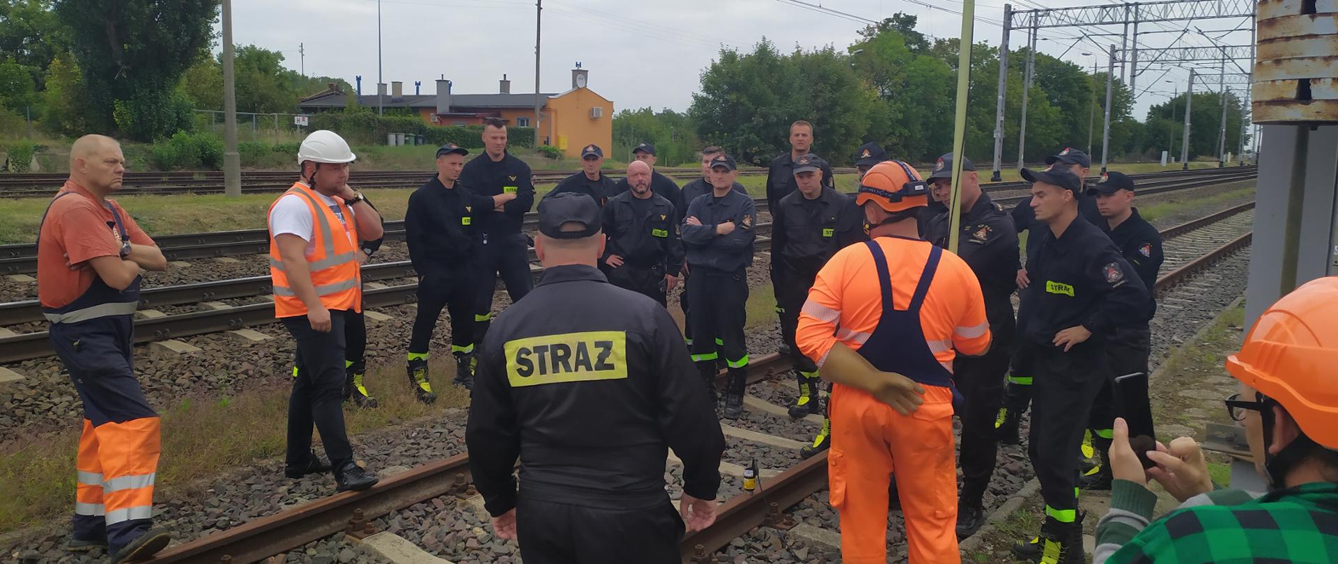 Strażacy wraz z pracownikami kolei stoją na torach podczas udzielanego instruktażu