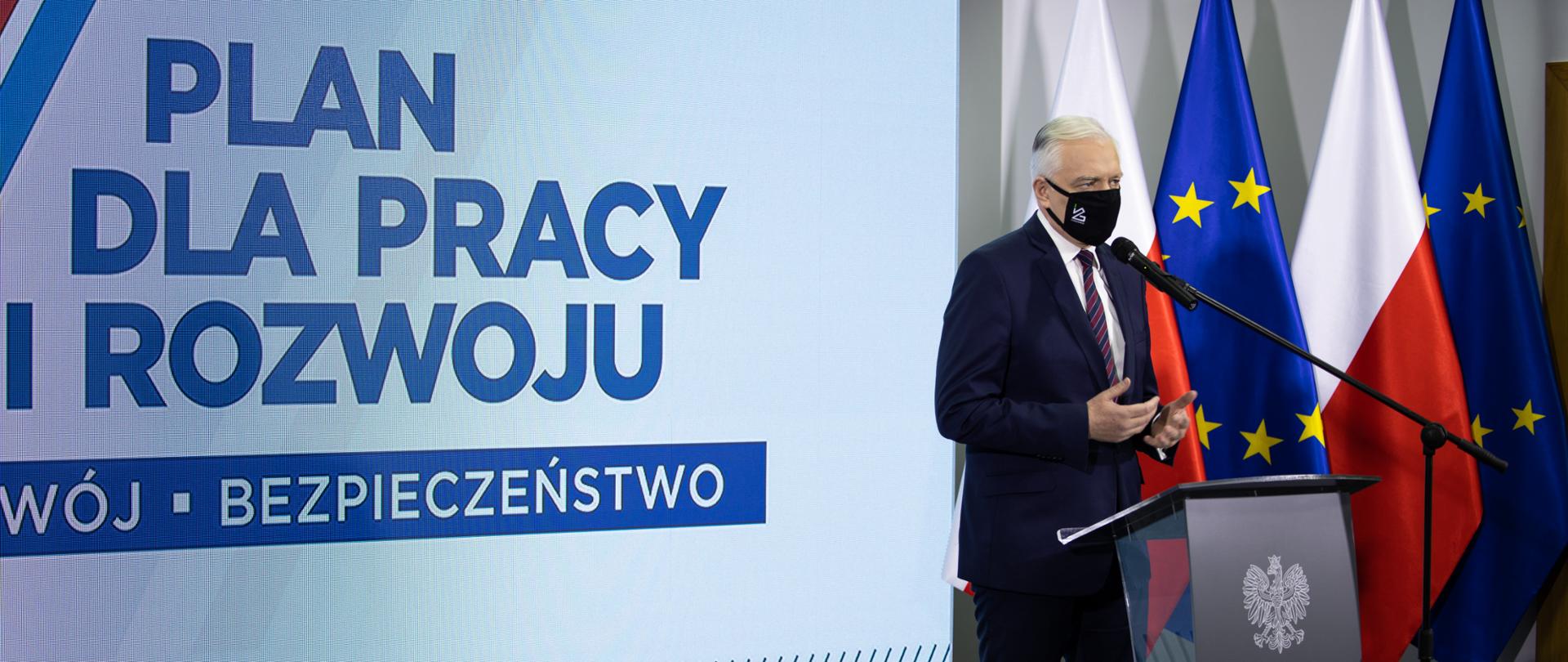 Wicepremier Jarosław Gowin podczas konferencji, na tle logotypu Planu dla Pracy i Rozwoju