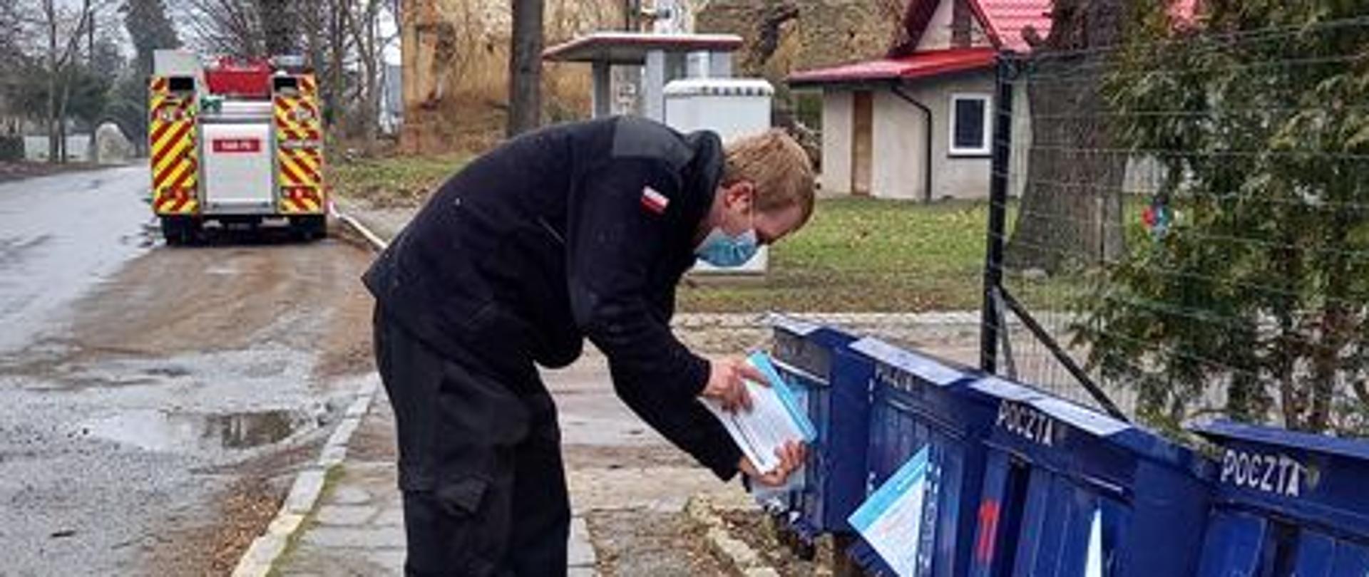 Strażak umieszcza ulotki w skrzynkach pocztowych