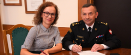 Pani Rektor i Pan Komendant, zajmując miejsca przy stole, podpisują porozumienie o współpracy, na dwóch egzemplarzach. 
