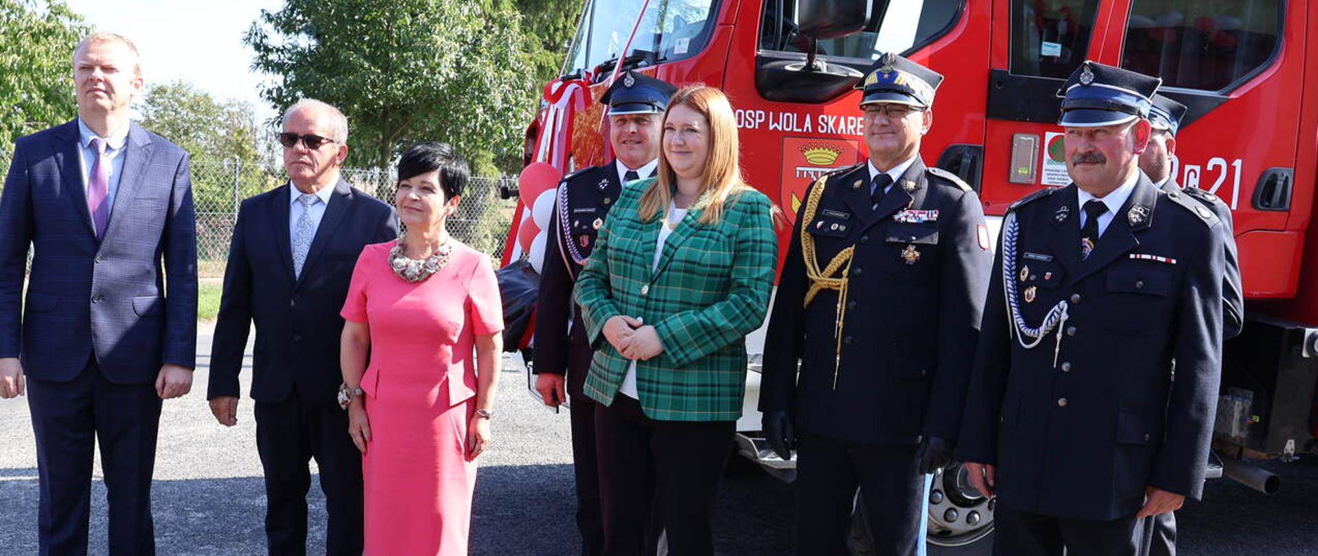 Zdjęcie na pierwszym planie przedstawia przedstawicieli administracji rządowej, Kujawsko-Pomorskiego Komendanta Wojewódzkiego oraz strażaków OSP. Na drugim planie wóz strażacki.