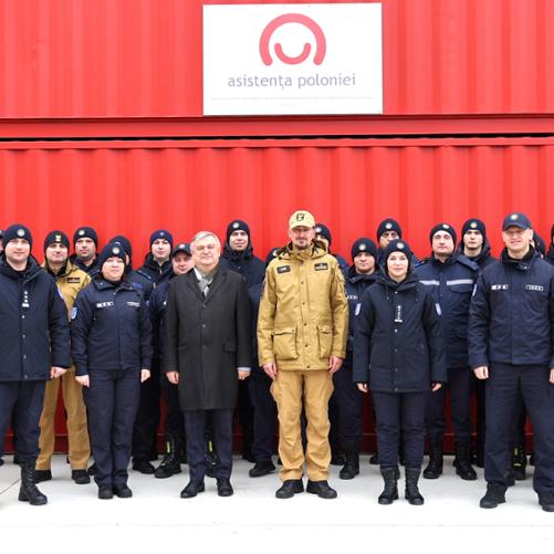 Grupowe zdjęcie uczestników szkolenia w służbowych mundurach na tle czerwonego kontenera z logo Polskiej pomocy po rumuńsku
