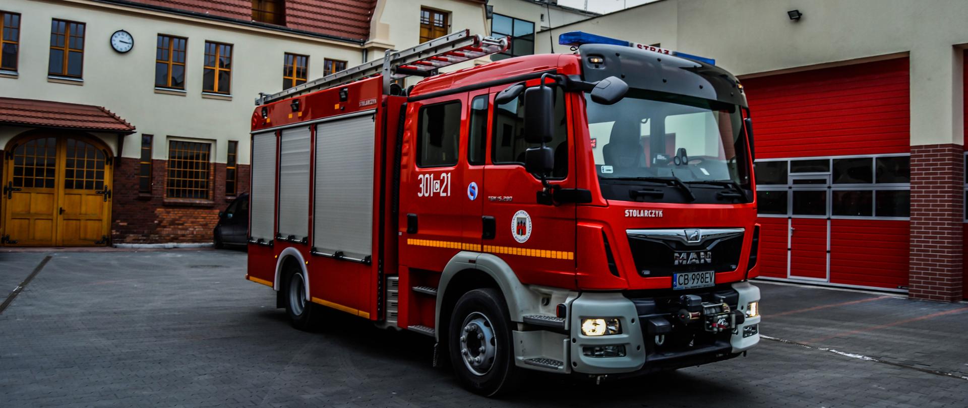 Samochód strażacki ciężarowy ratowniczo-gaśniczy Jednostki Ratowniczo-Gaśniczej nr 1 w Bydgoszczy, podwozie marki Man, w tle budynek jednostki.