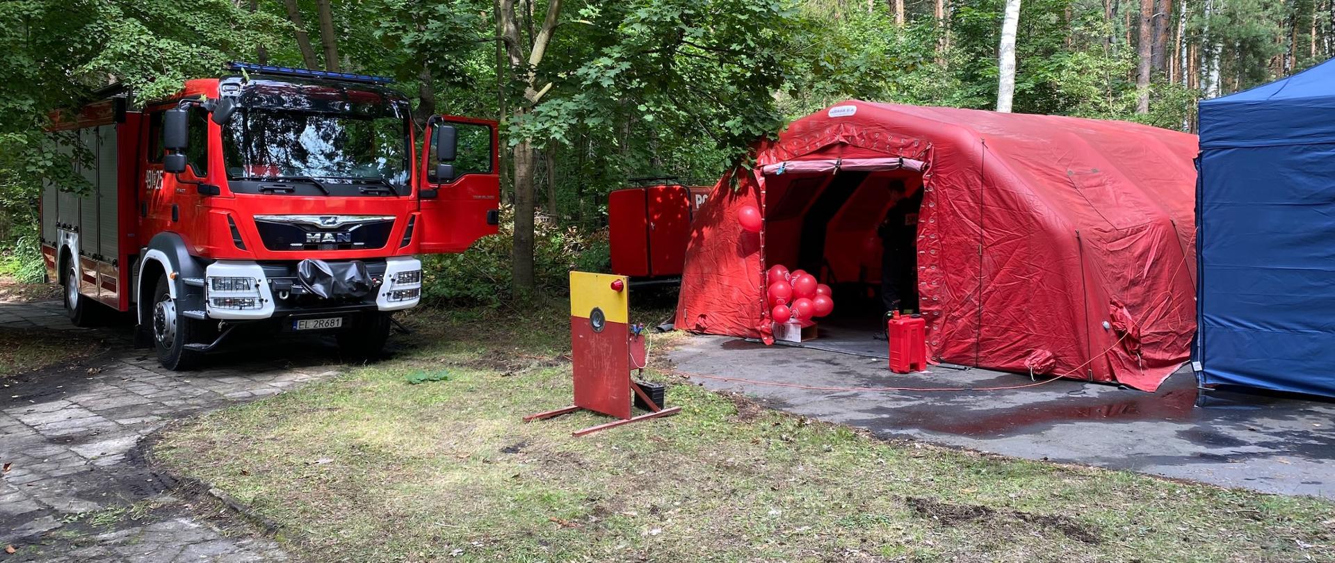 Samochód strażacki i czerwony namiot stoją w lesie